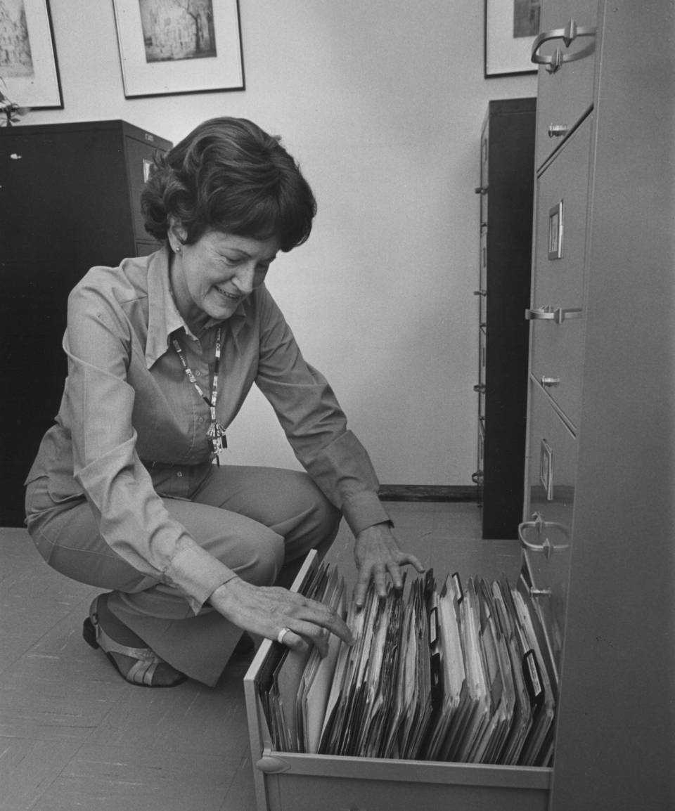 A woman kneeling beside the open drawer of a filing cabinet