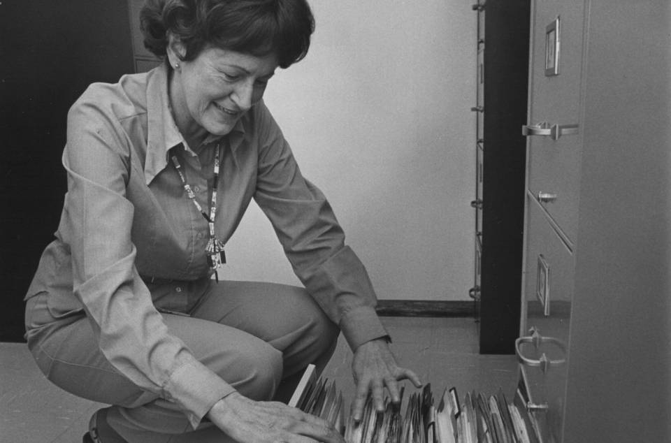 A woman kneeling beside the open drawer of a filing cabinet