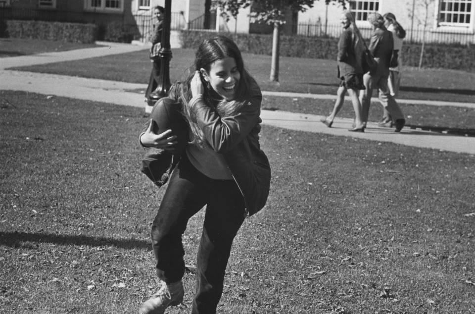 A young woman holding a football and smiling, with other students in the background