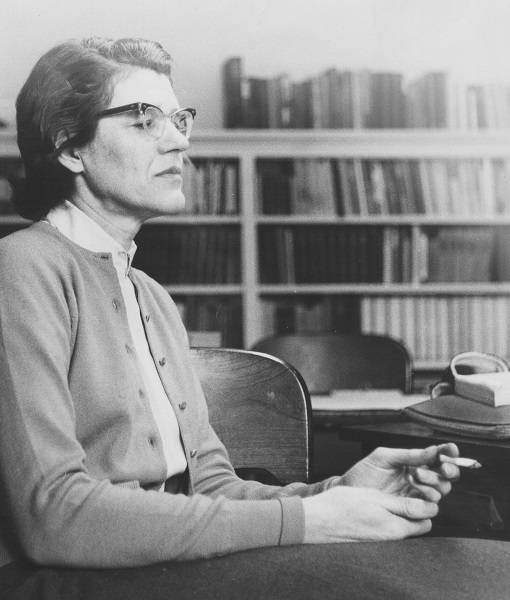 Professor Margaret Jane Sinden holding a cigarette, in front of bookshelves