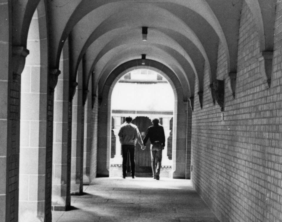 Covered walkway in University College quadrangle, with two men walking hand in hand