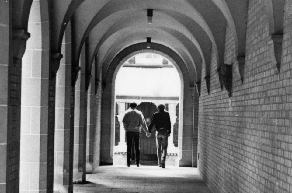 Covered walkway in University College quadrangle, with two men walking hand in hand