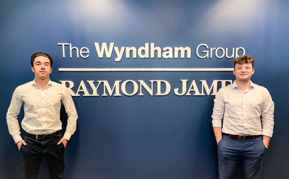 Edouard Larouche standing in front of Wyndhan Group sign with teammate 