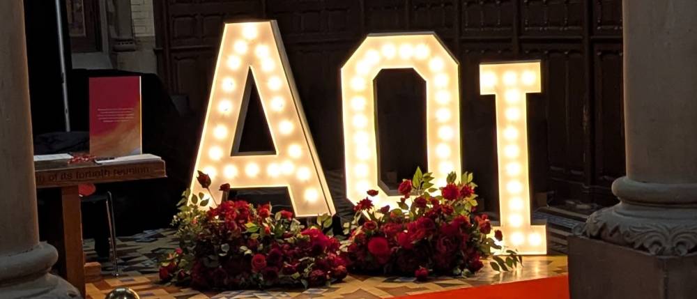 A red carpet path through the opening stone pillars at UC leads to a lit-up sign reading AOI