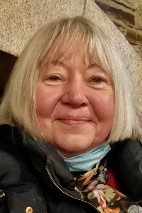 Portrait of Laurie Dennett, her smiling face framed with a white bob and pale blue scarf