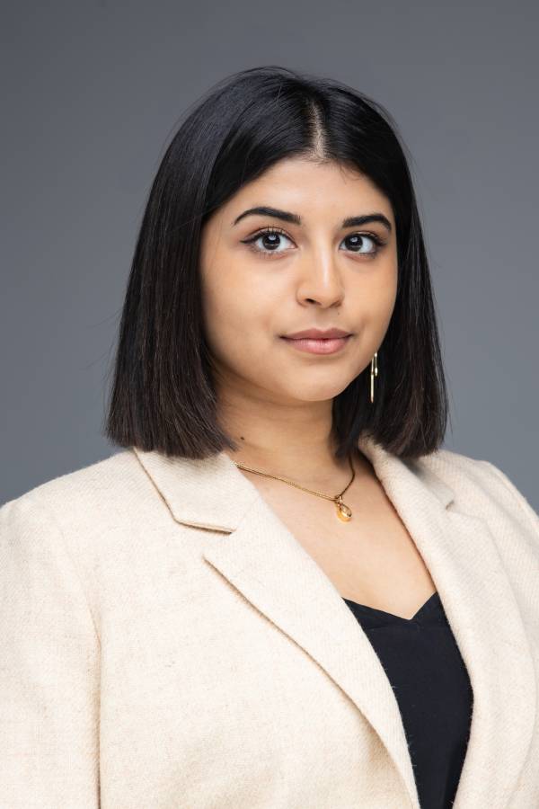 Portrait of Uma Kalkar in a beige blazer and black top. Her smile is slight and her black hair falls neatly to her shoulders.