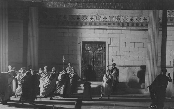 About a dozen actors performing on stage in classical costume