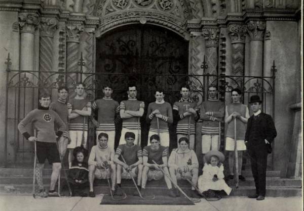 thirteen young men with lacrosse sticks, one man in a suit, and two small children
