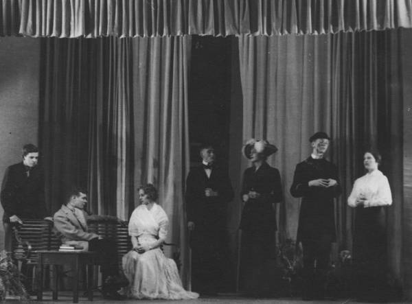 Seven actors on stage in period costumes