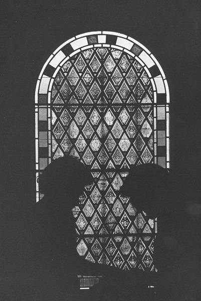 Silhouettes of two people seemingly holding books, in front of stained glass window