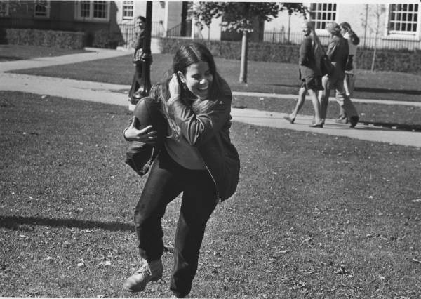 A young woman holding a football and smiling, with other students in the background