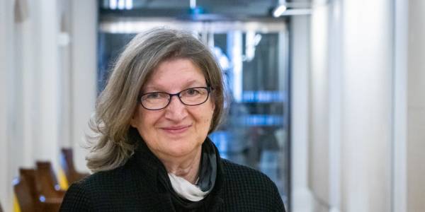 Barbara Fischer wearing black-rimmed glasses, standing in front of a glass doorway