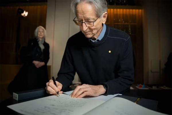 Geoffrey Hinton signs the guest book at the Nobel Prize Museum