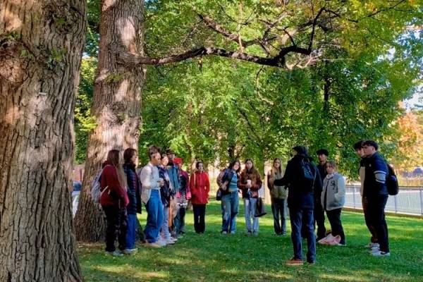 students and alan ackerman standing in a circle beside a large tree