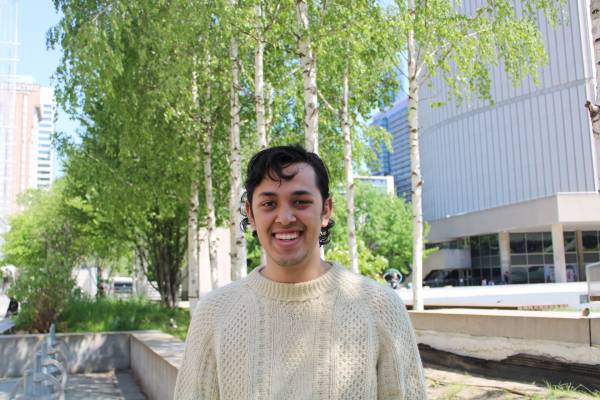 Student Cameron Miranda-Radbord is smiling in front of trees and is wearing a beige wool sweater. 