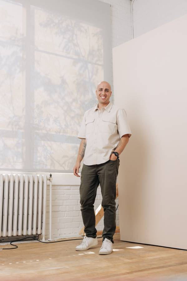 A man in casual clothes smiles of the camera in an empty room