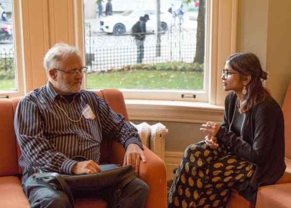An alumni mentor and student mentee sit across from each other on a couch, talking