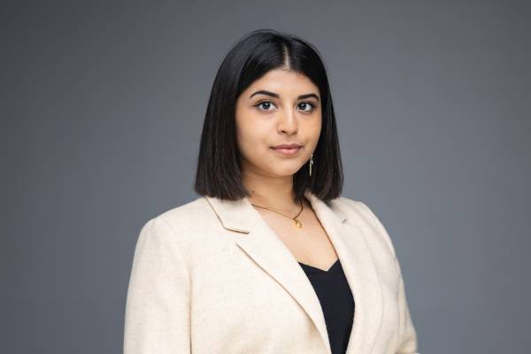 Portrait of Uma Kalkar in a beige blazer and black top. Her smile is slight and her black hair falls neatly to her shoulders.