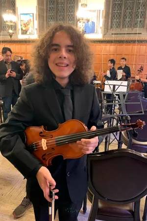 Honciuc Menendez holding a violin inside the hart house concert hall, wearing full concert blacks.