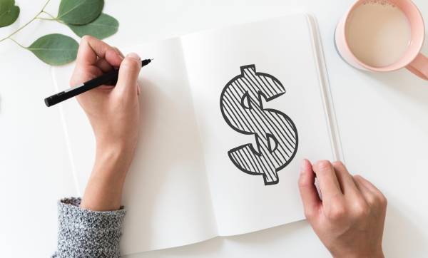 Left-handed student drawing a money sign in a notebook