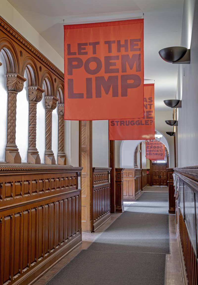 UC hallway with flag on ceiling reading "Let the Poem Limp"