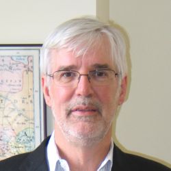 Headshot of Alan Bewell, wearing a black suit and glasses.