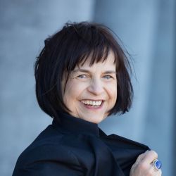 Banuta Rubess, wearing a black jacket smiling at the camera.
