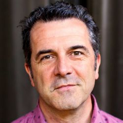 Guillermo Verdecchia, wearing a pink shirt, and smiling at the camera