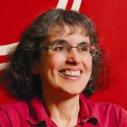 Keren Rice, Smiling off to the side of the camera, wearing glasses and a red shirt.