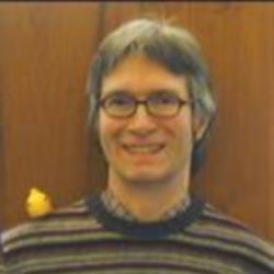 Joe Repka, smiling at camera, wearing glasses and a brown striped sweater.