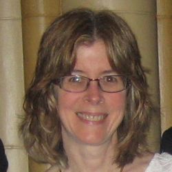 Suzanne Stevenson headshot, smiling at the camera with red-framed glasses, a white shirt, and a gold necklace on.