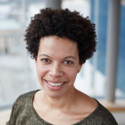 Headshot of Seika Boye, smiling at the camera, wearing a brown-grey shirt.