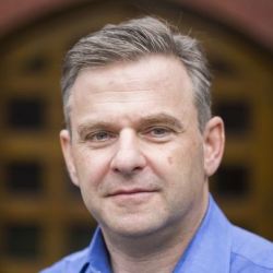 Robert Steiner, wearing a blue shirt, staring off to the side of the camera.