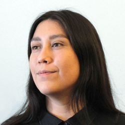 Headshot of indigenous-canadian woman with long dark hair, copper skin, wearing a black button-up blouse