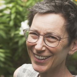 Jane Wolff, smiling at the camera, wearing glasses and a gray shirt.