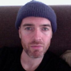 Micheal Cobb staring at the camera with a grey hat and black T-shirt on>