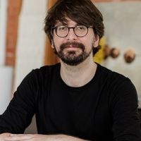 Alex Djedovic, wearing a black shirt and black glasses, staring at the camera.