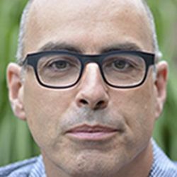 Sean Hawkins, staring at the camera with black glasses on and a blue-white checkered shirt.