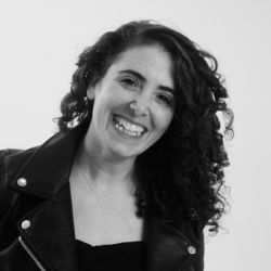 Laine Halpern Zisman, wearing a black shirt and leather jacket, smiling at the camera.