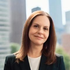 Vikki Visvis, smiling at the camera, with a black jacket and white shirt on.