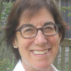 Headshot of Christina Kramer smiling at the camera, wearing black glasses and a white shirt.