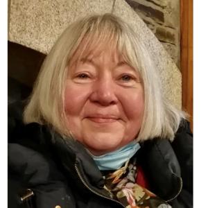 Portrait of Laurie Dennett, her smiling face framed with a white bob and pale blue scarf