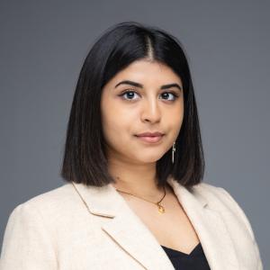 Portrait of Uma Kalkar in a beige blazer and black top. Her smile is slight and her black hair falls neatly to her shoulders.