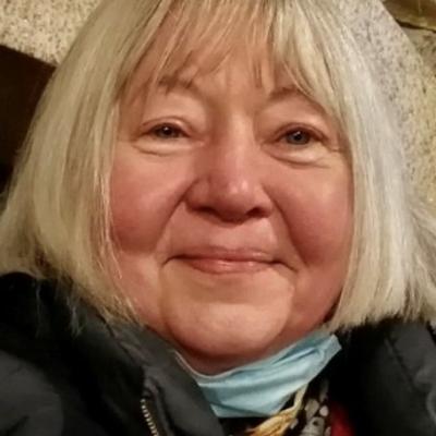 Portrait of Laurie Dennett, her smiling face framed with a white bob and pale blue scarf