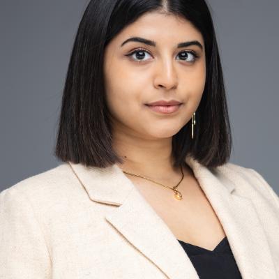 Portrait of Uma Kalkar in a beige blazer and black top. Her smile is slight and her black hair falls neatly to her shoulders.